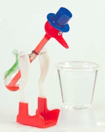 a drinking bird positioned over a small plastic cup of water